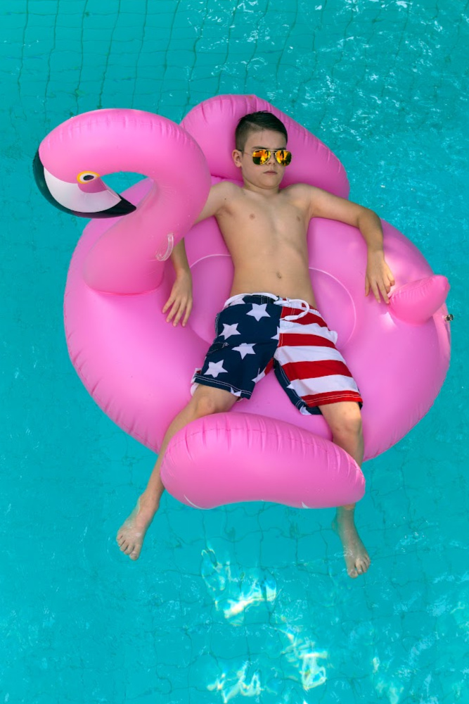 Young boy on a pink flamingo floating in the pool Young boy on a pink flamingo floating in the pool